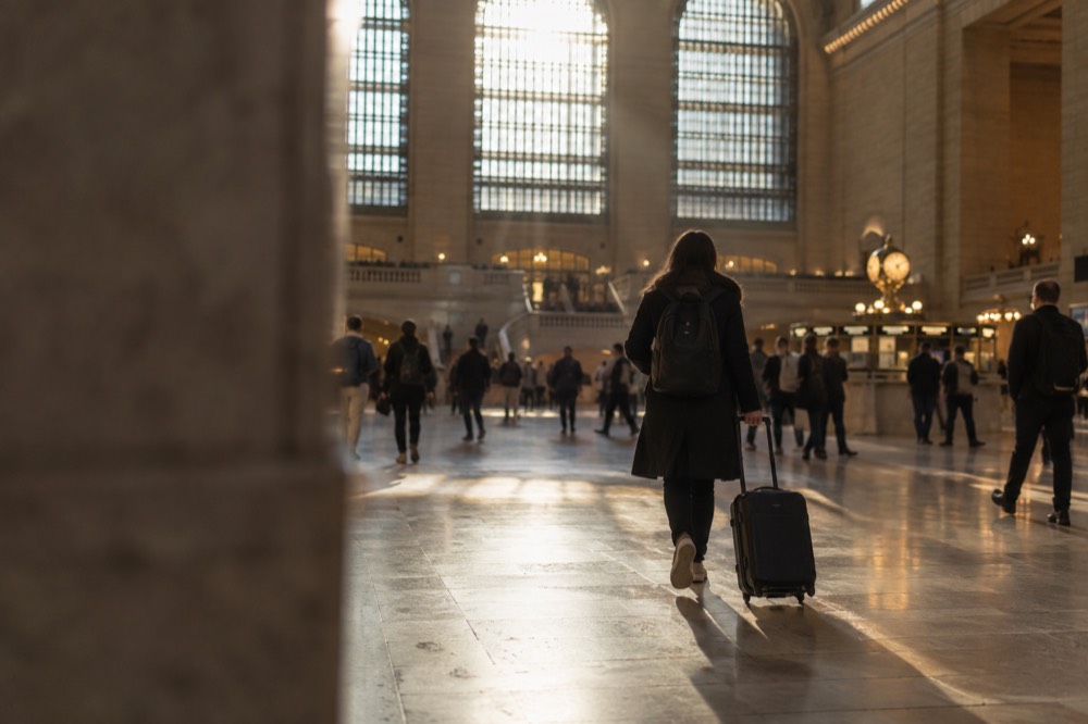 A traveler pulling a suitcase across the main concourse of Grand Central Terminal beneath its arched windows