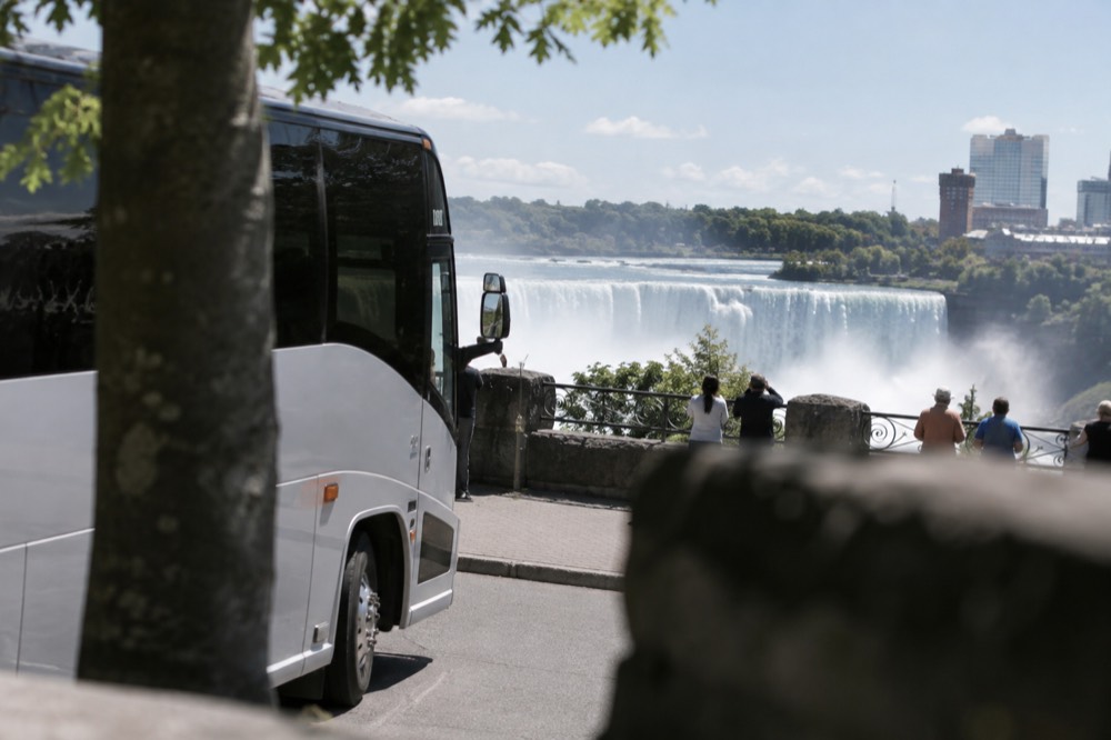 A coach parked near the Niagara Falls overlook area with the falls visible in the background