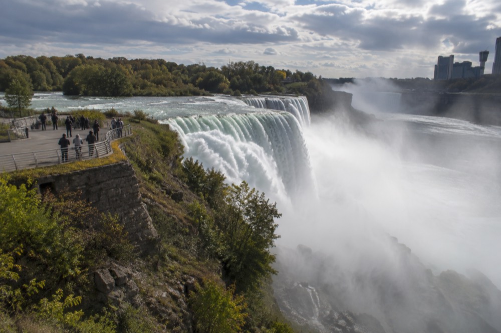 A wide waterfall plunging into a misty gorge with a viewing platform along the railing