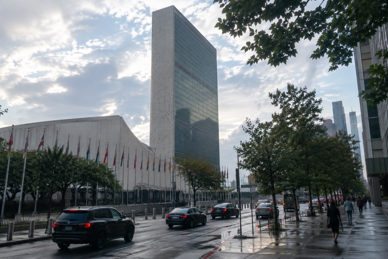 The United Nations Headquarters complex beside the East River, with the Secretariat tower and member state flags along 1st Avenue