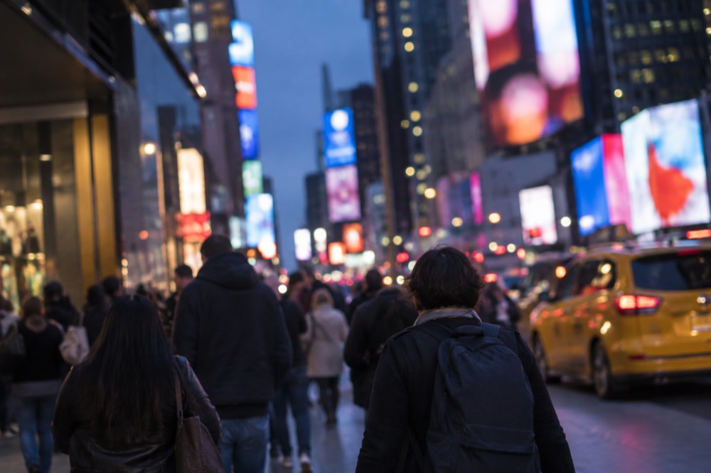 A crowded sidewalk in Times Square at dusk with yellow taxis and glowing billboards.