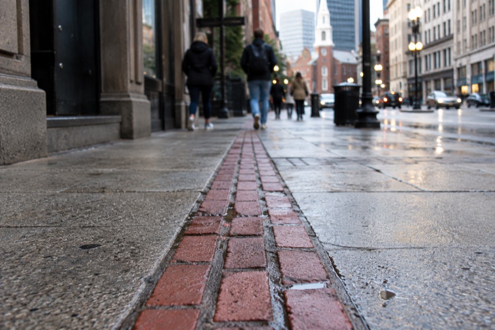 A red-brick Freedom Trail marker set into a sidewalk in downtown Boston