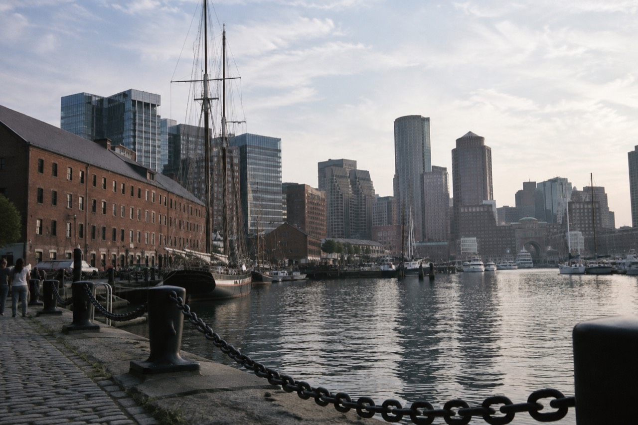 Boston's waterfront with historic brick buildings and masted ships along the harbor