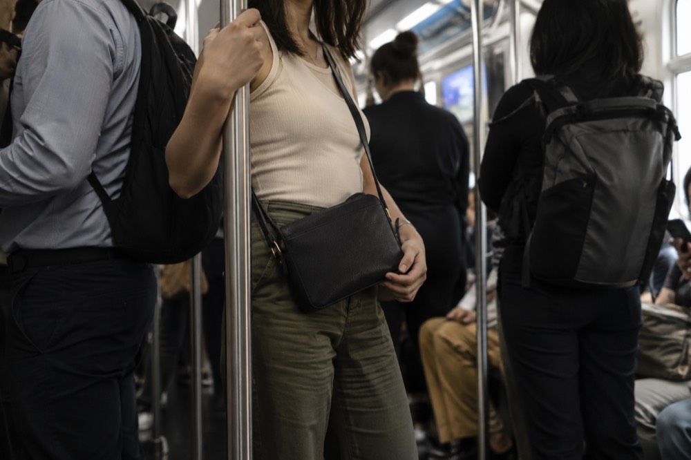 A crossbody purse held in front of a rider on a crowded New York subway train