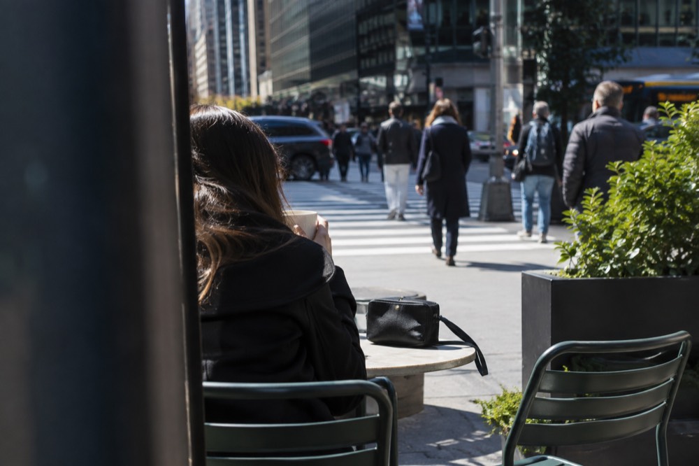 A small zippered crossbody bag resting on a cafe table beside a coffee cup