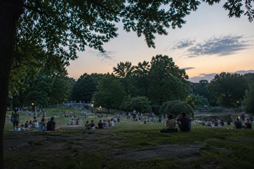 Sunbathers on a crowded Central Park lawn under a bright summer sky