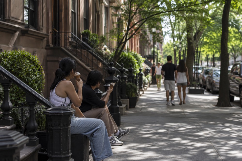 People eating ice cream cones on a shaded brownstone street in summer