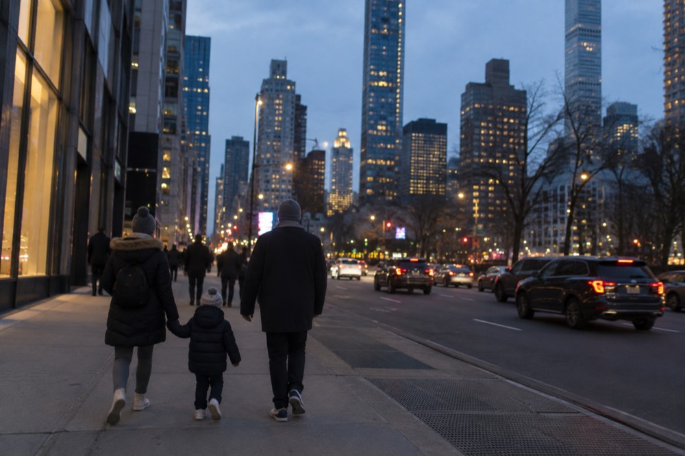 A family walking along a wide New York sidewalk with the skyline behind them