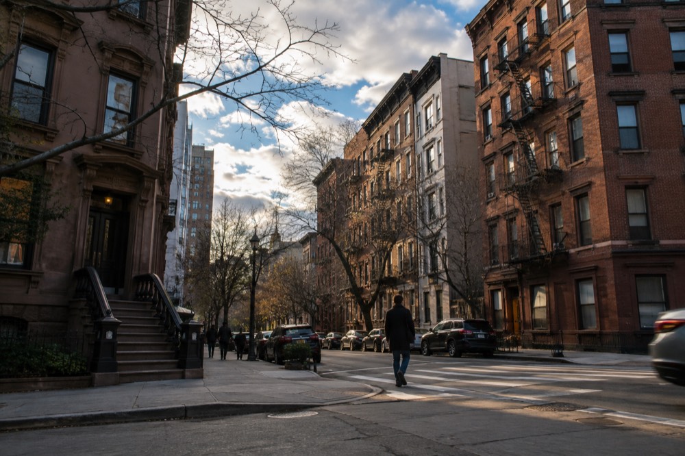 A quiet New York City street corner in the late afternoon with brownstone buildings and a pedestrian crossing