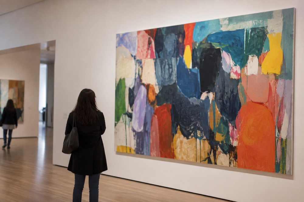 A gallery visitor standing in front of a large colorful modern painting in a bright museum room