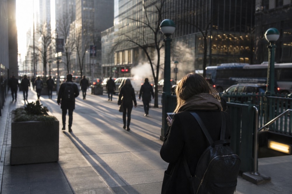 A visitor checking a phone map while standing on a busy New York sidewalk with skyscrapers behind