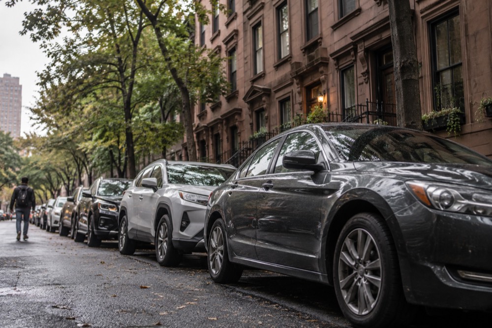 A row of parked cars along a narrow New York City street with a brownstone building behind them