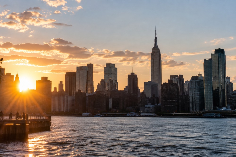 The Manhattan skyline seen across water at golden hour, with the Empire State Building rising above neighboring towers.
