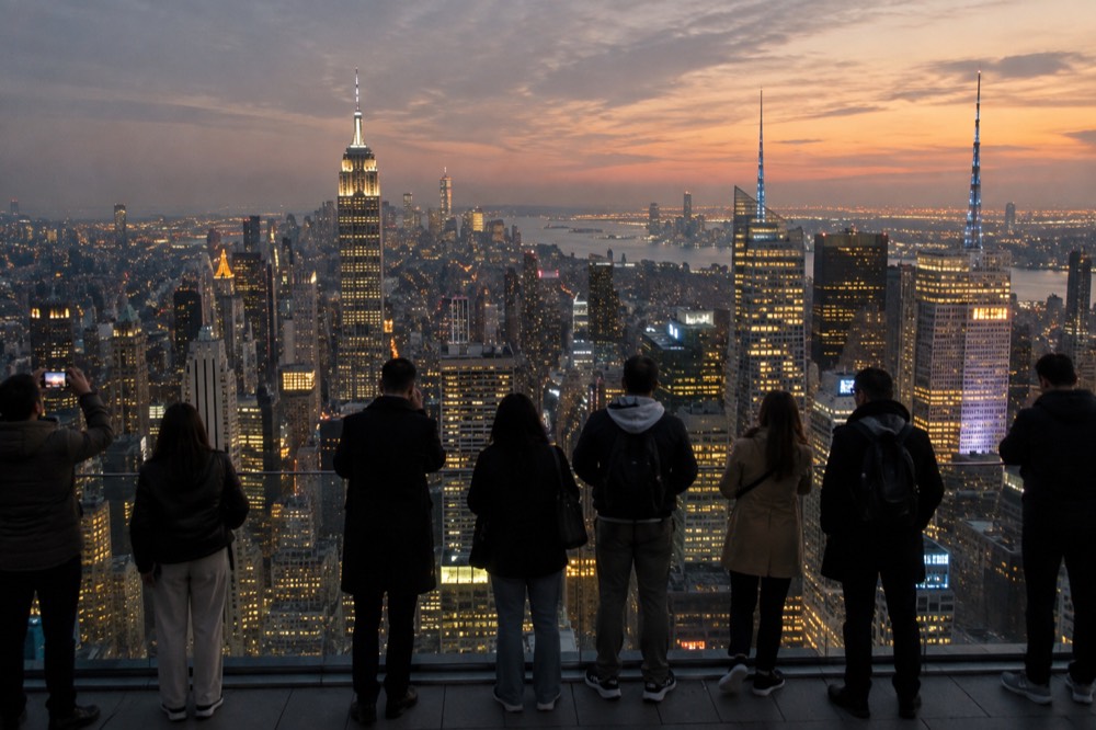An observation deck at dusk with visitors at the rail and the city grid glowing below.