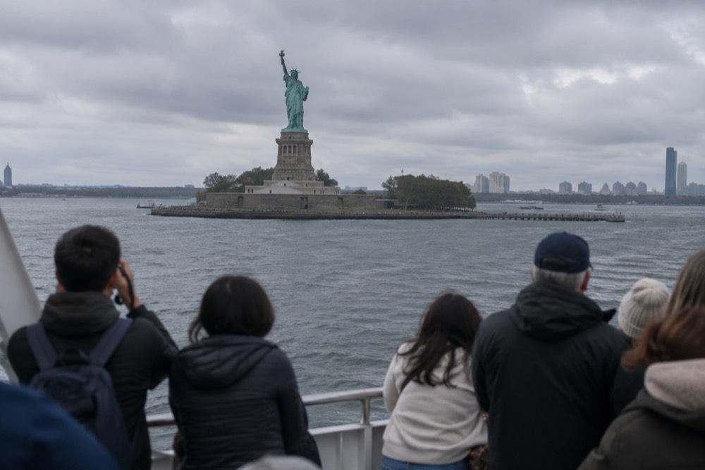 The Statue of Liberty seen from a ferry deck, with visitors at the rail