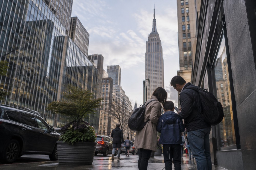 A family checking a phone on a Midtown sidewalk with the Empire State Building behind them