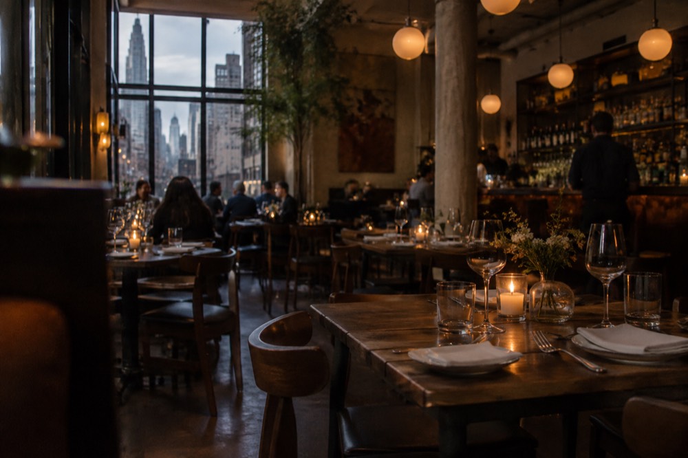 A candlelit downtown Manhattan restaurant dining room with set tables and a bar in the background