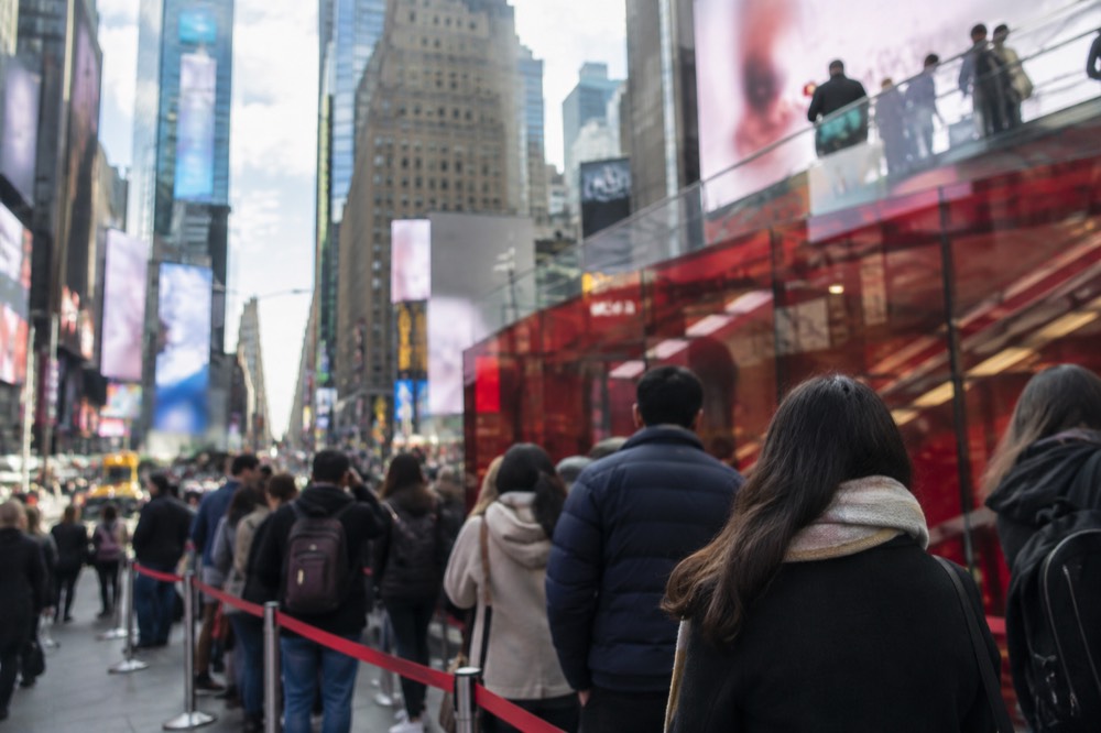 A crowd of theatergoers queuing at a red glass TKTS discount ticket booth in Times Square