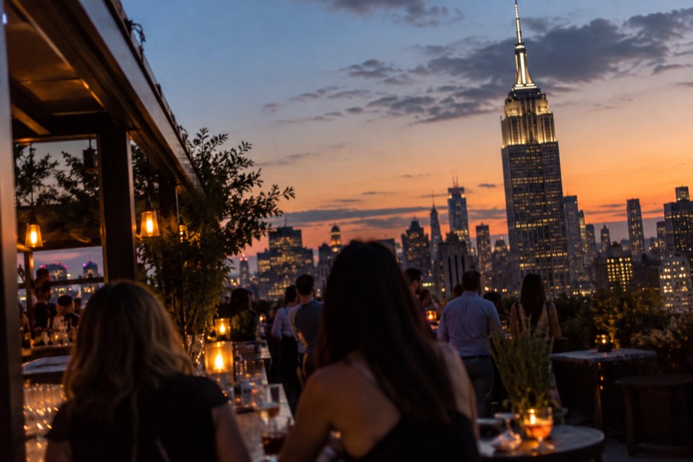 A rooftop bar at dusk with the Empire State Building lit up in the background
