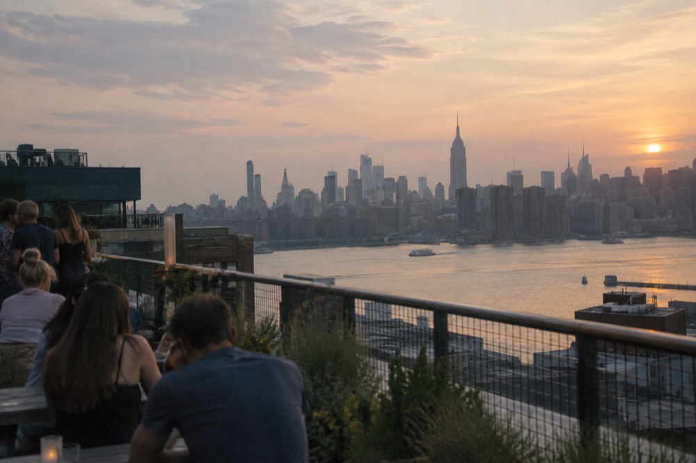 A rooftop terrace in Williamsburg, Brooklyn, at sunset with the Manhattan skyline and the Empire State Building across the water