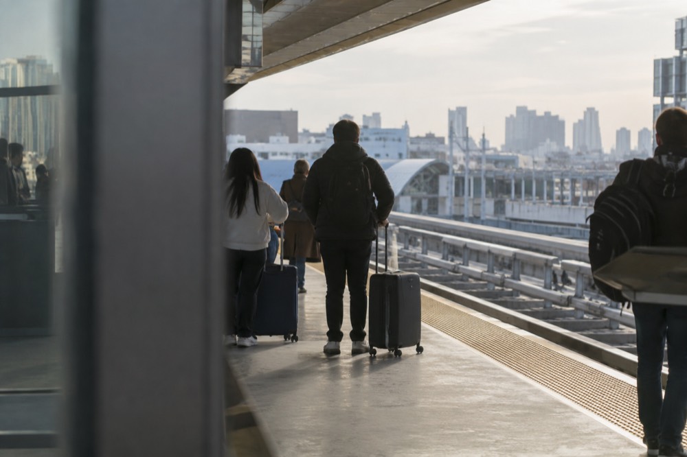 Travelers with suitcases waiting on an AirTrain platform at Jamaica Station in Queens
