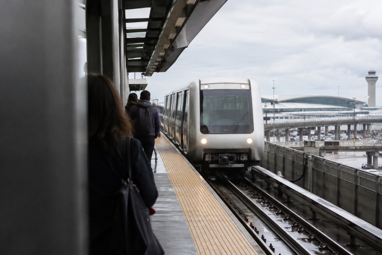 An AirTrain car arriving at a JFK Airport station platform with terminal signs overhead