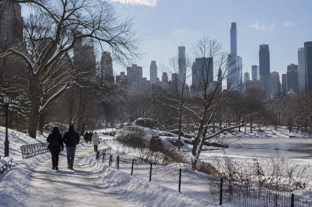 A snow-covered Central Park path with bare trees and the Manhattan skyline in the distance