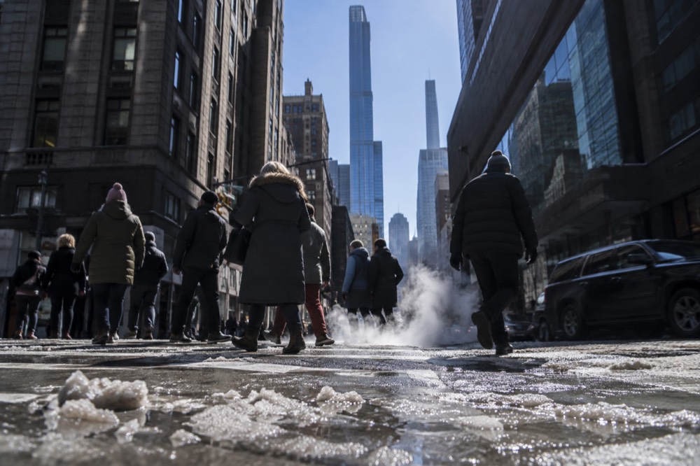 Pedestrians in winter coats crossing a slushy Manhattan street with steam rising from the pavement