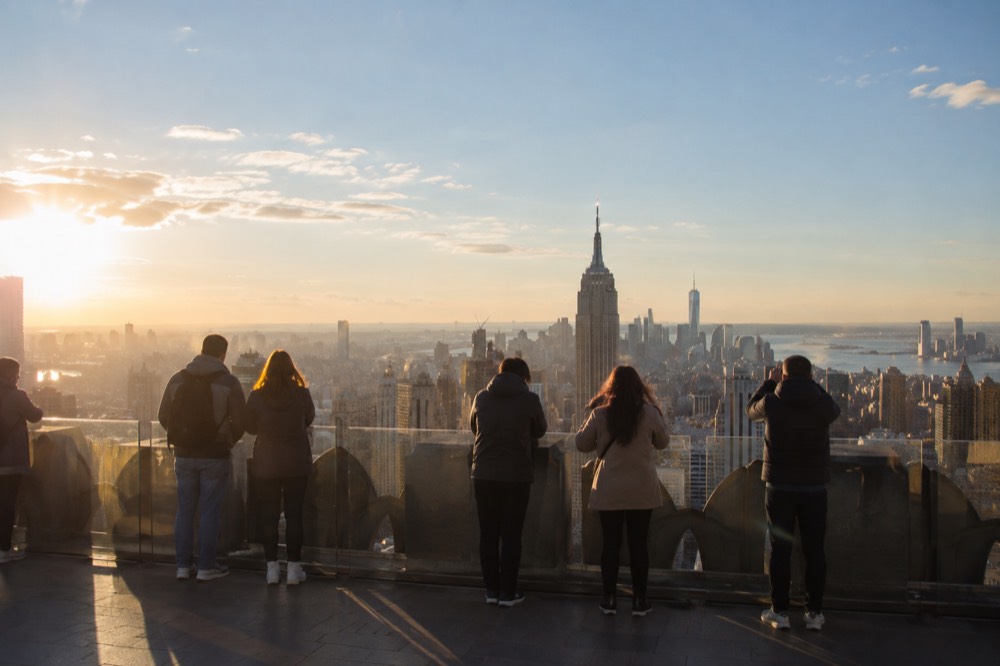 Visitors looking at the Manhattan skyline from an observation deck on a clear afternoon
