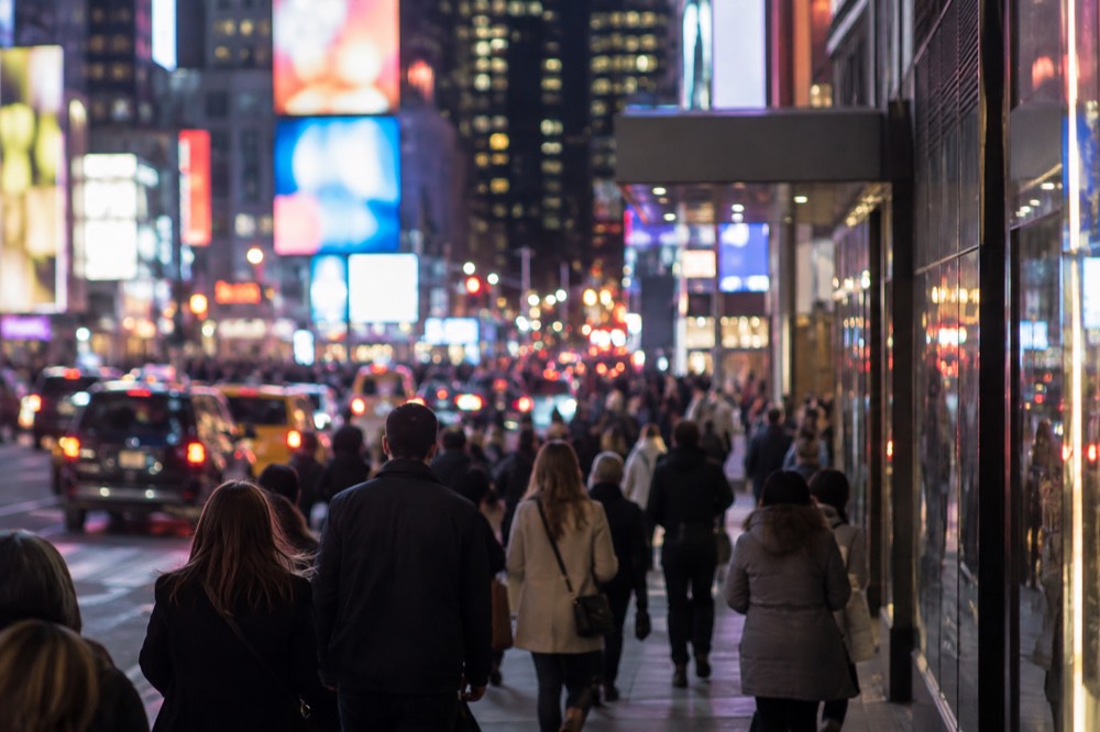 A crowded sidewalk in the Theater District at night with theatergoers walking under glowing marquee lights