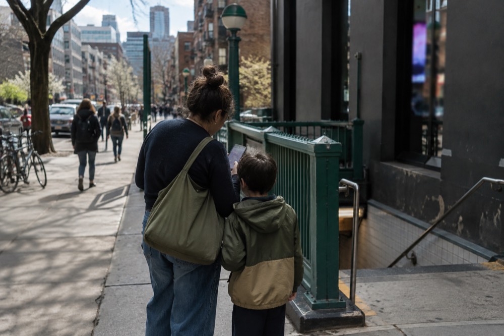 A parent and child checking a phone calendar outside a Brooklyn subway entrance