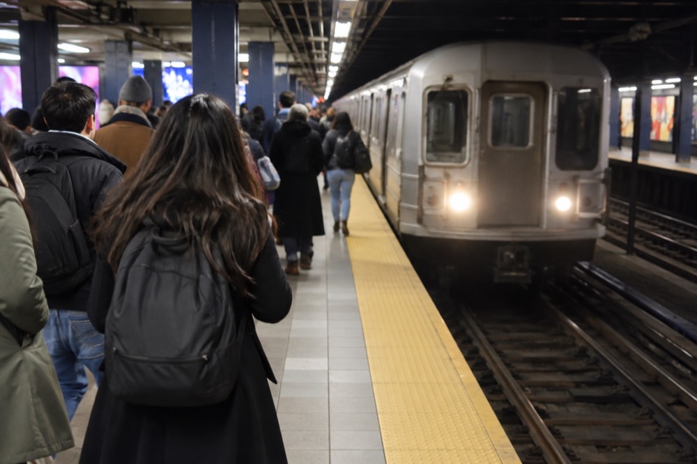 A crowded subway platform at Times Sq-42 St with a train arriving and passengers waiting near the edge