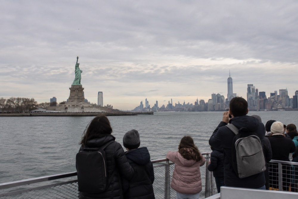 A ferry boat crossing the harbor toward the Statue of Liberty with families at the rail
