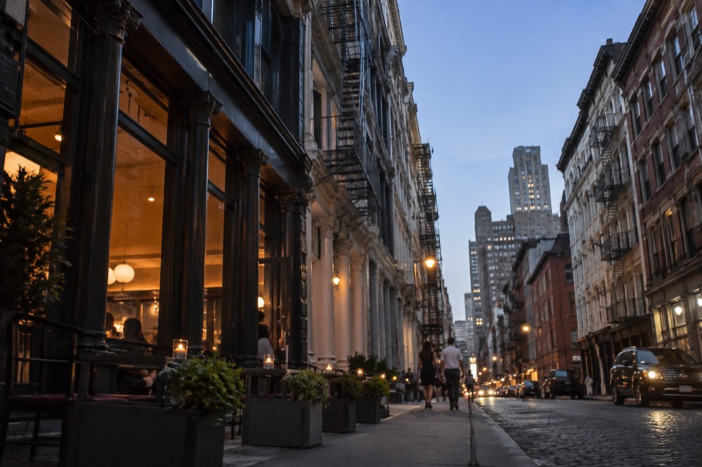 A narrow SoHo street at dusk with cast-iron building facades and restaurant awnings