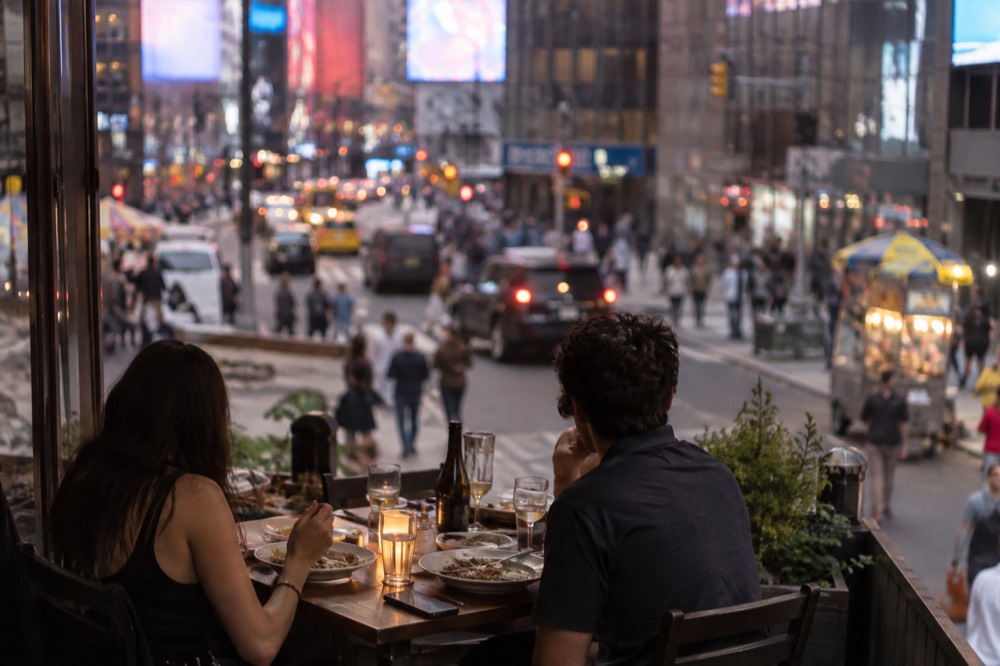 Diners seated at a small restaurant table in Hell's Kitchen in the early evening