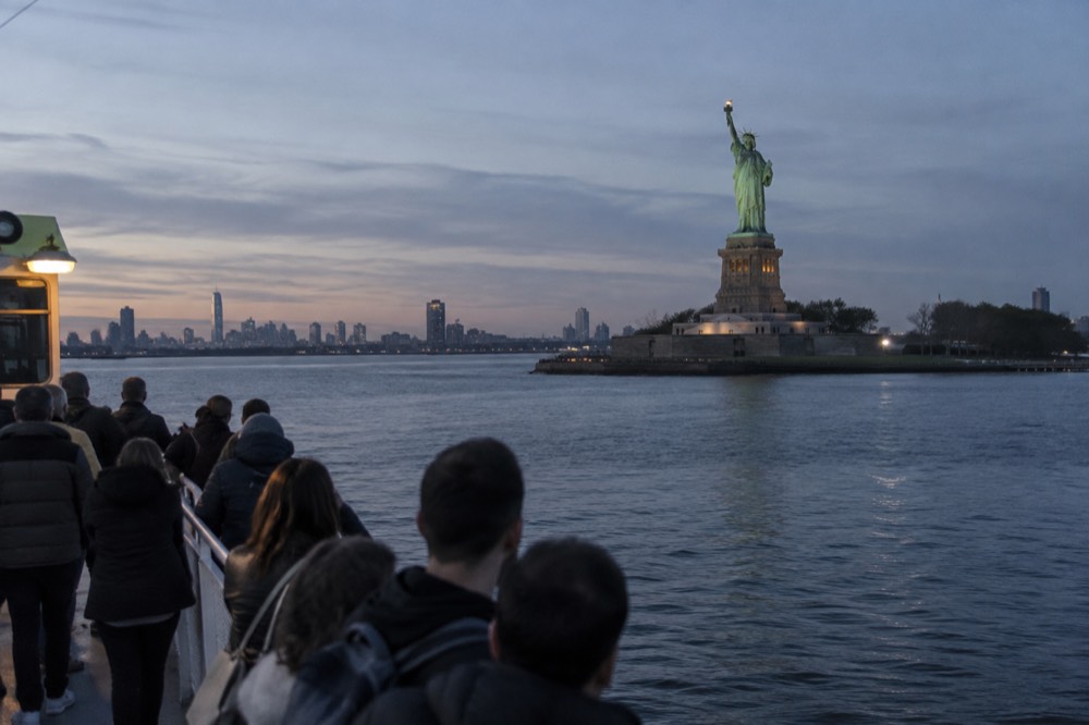 A passenger ferry crossing New York Harbor toward the Statue of Liberty on a clear morning