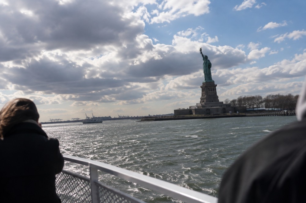 The Statue of Liberty seen from the water with a ferry railing in the foreground