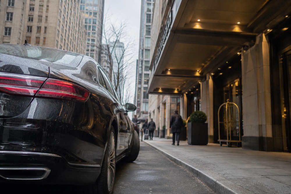 A parked car beside a hotel entrance on a narrow New York street with tall buildings above