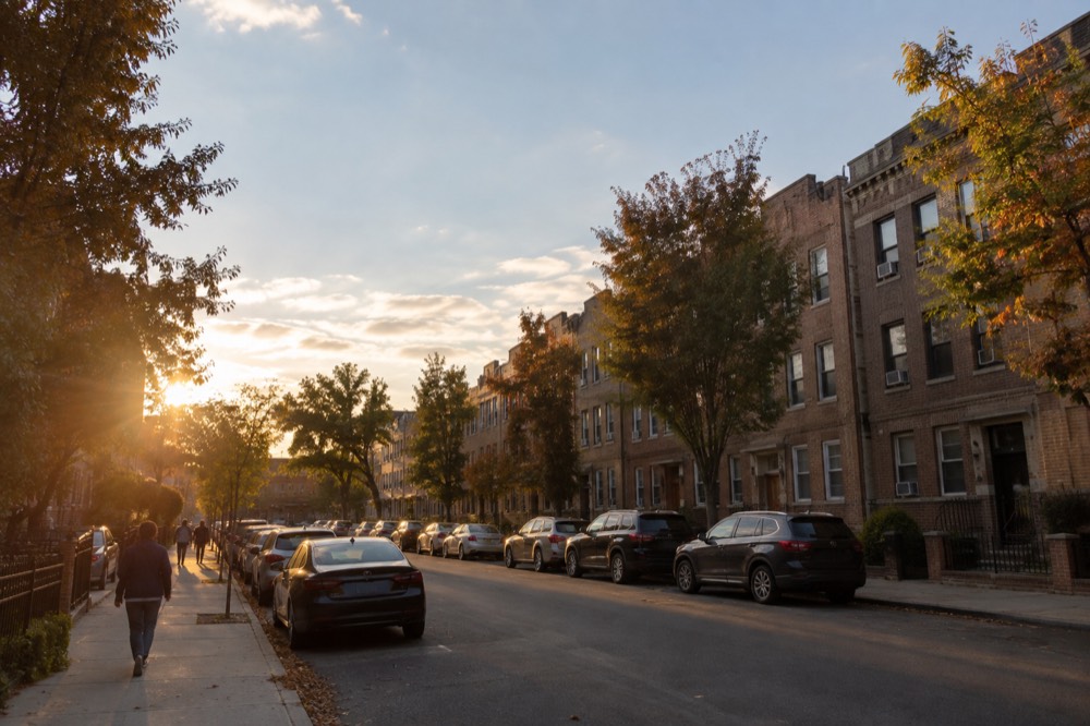 Row of low-rise brick apartment buildings along a quiet street in Astoria, Queens, under a late afternoon sky