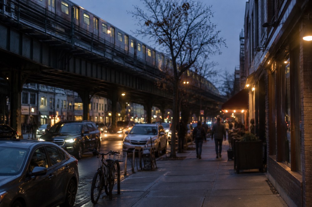 Elevated subway tracks running above a commercial street with awnings and small shops in Astoria