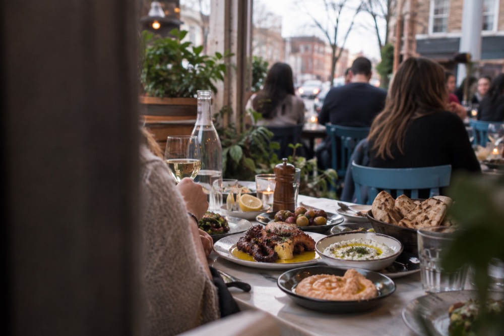 A table of meze dishes, including grilled octopus, dips and bread, at a busy Greek restaurant in Astoria