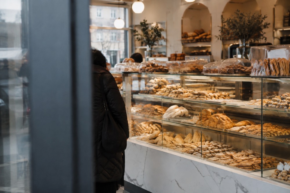 A glass display case of pastries and breads inside a bright Greek bakery in Astoria