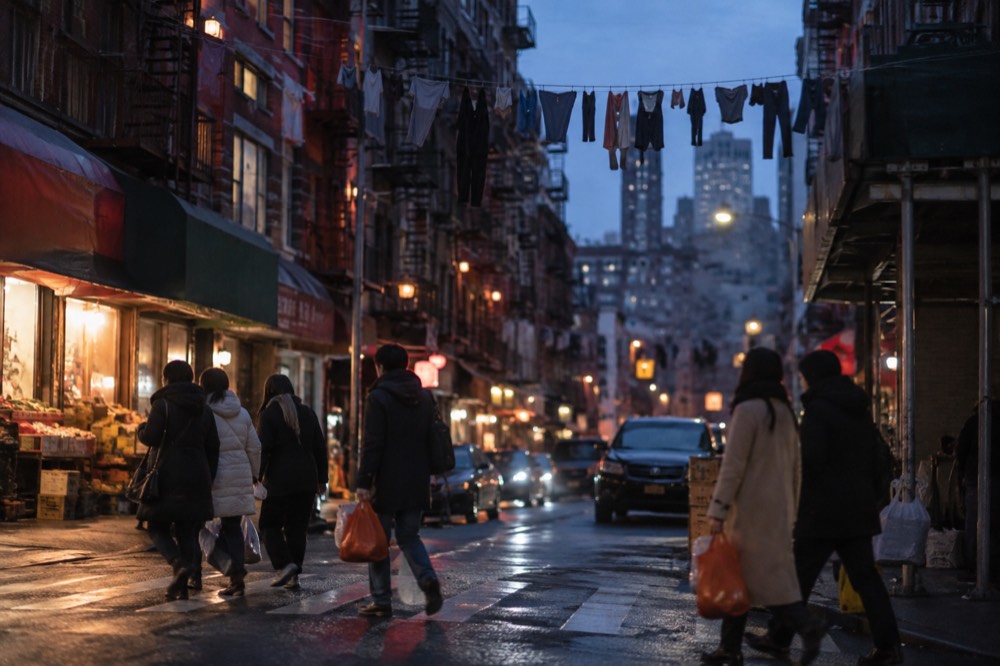 Shoppers crossing a narrow intersection in Chinatown beneath hanging laundry and signage