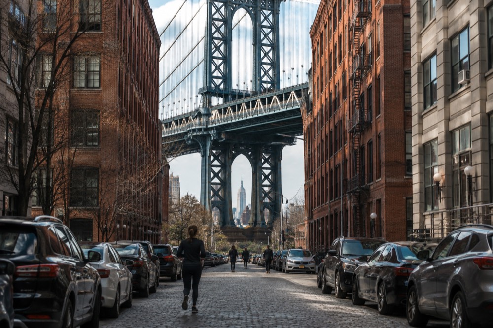 The Empire State Building framed inside the Manhattan Bridge arch above a cobblestone street in Dumbo