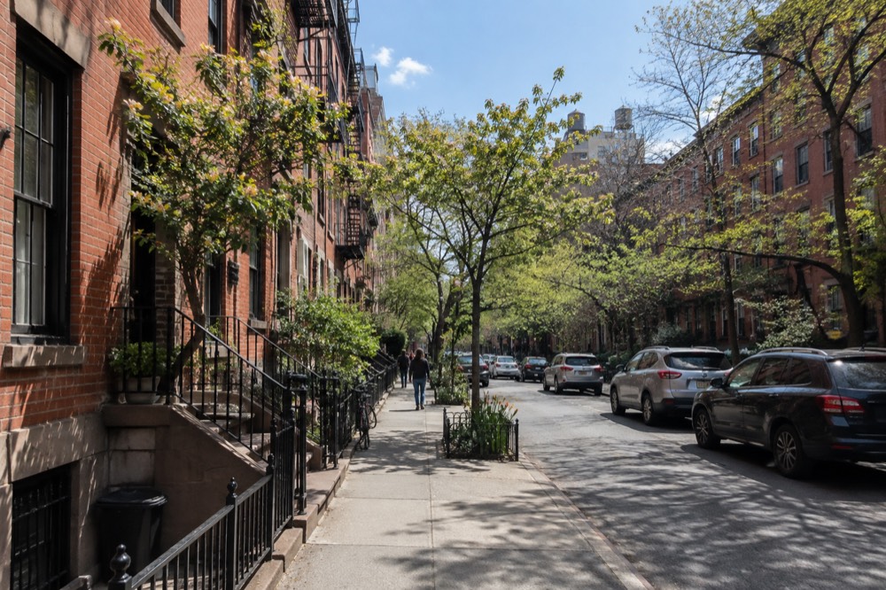 A tree-lined East Village street with low brick buildings, awnings and a corner restaurant at dusk