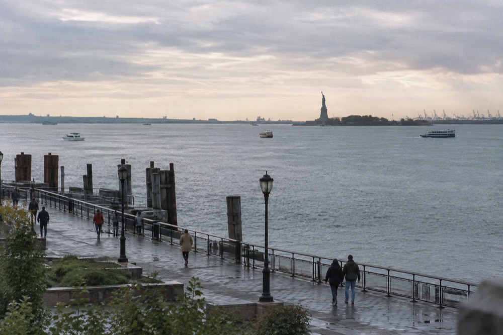 The harbor esplanade at the southern tip of Manhattan with the Statue of Liberty visible in the distance