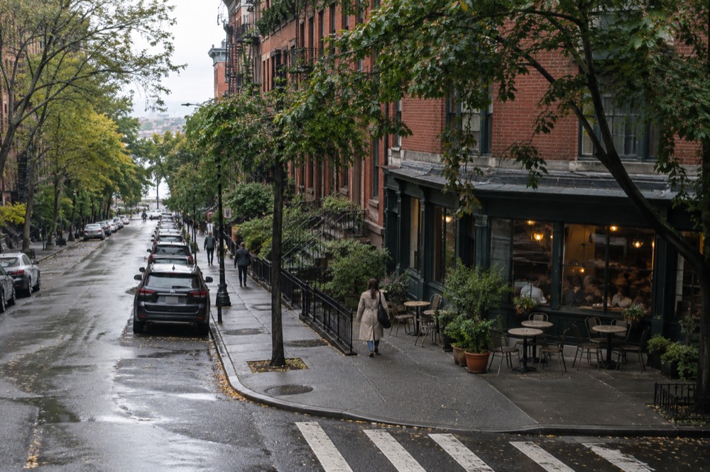 Tree-lined Greenwich Village street with brick row houses and a corner cafe
