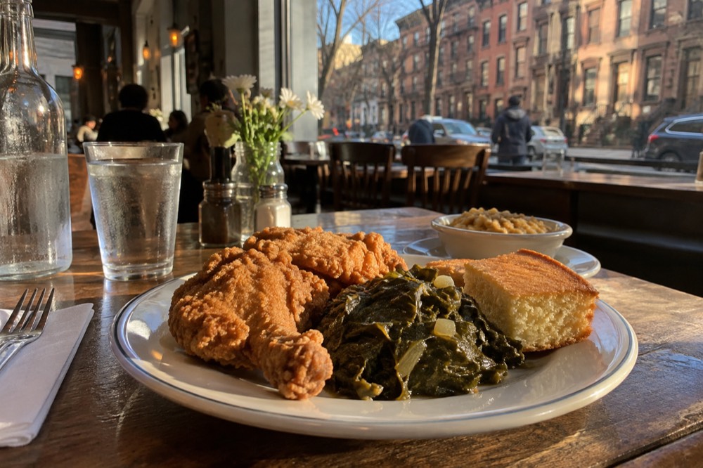 A plate of fried chicken, collard greens and cornbread on a restaurant table in Harlem