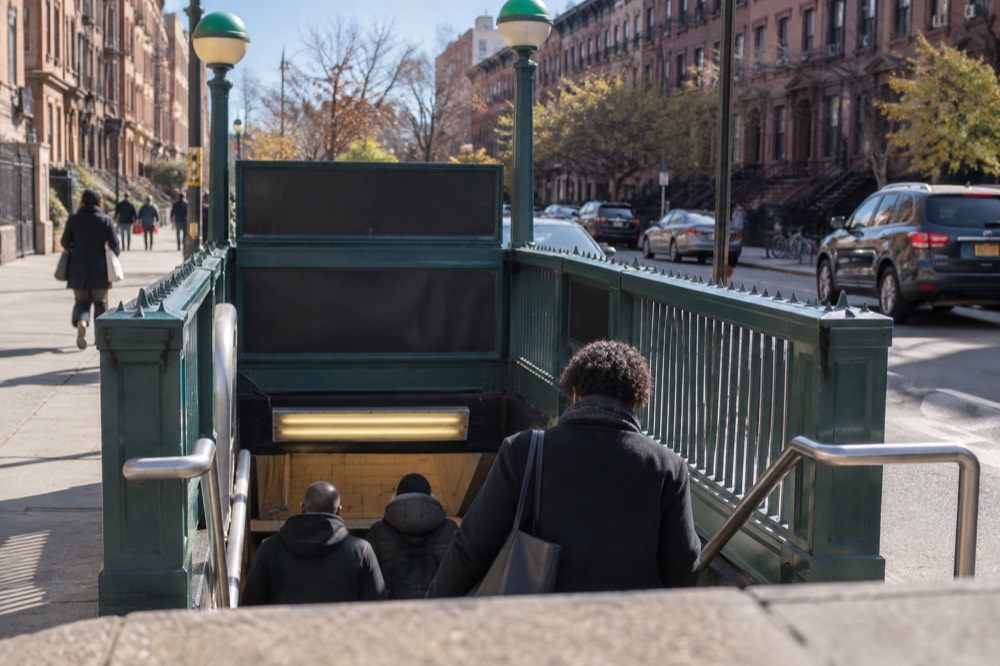 A New York subway entrance on a Harlem corner with passengers descending the stairs