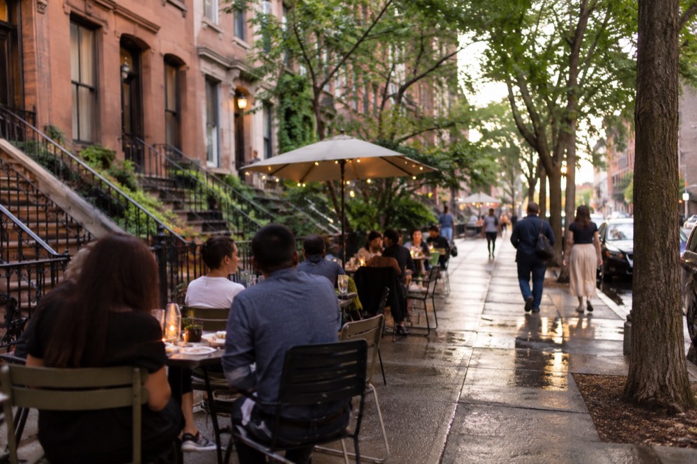 People dining at outdoor tables on a Harlem street in the early evening